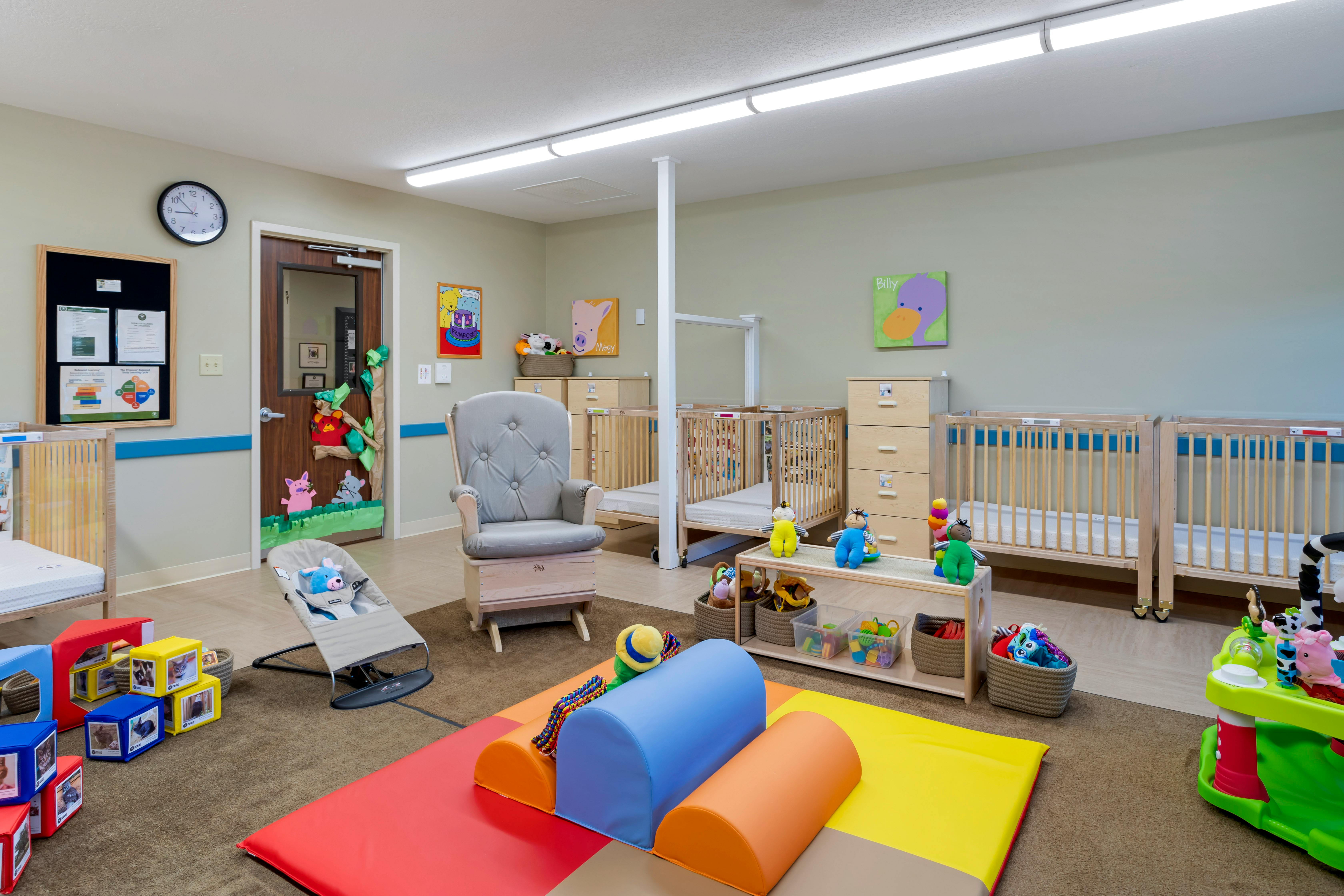 A colorful childcare classroom with cribs, play mats, and a rocking chair