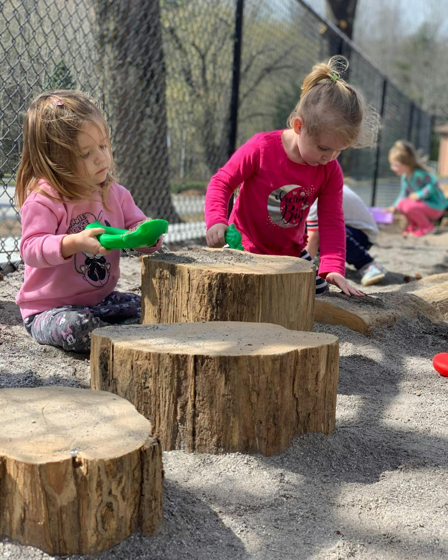 Two children playing with sand and tree stumps outdoors