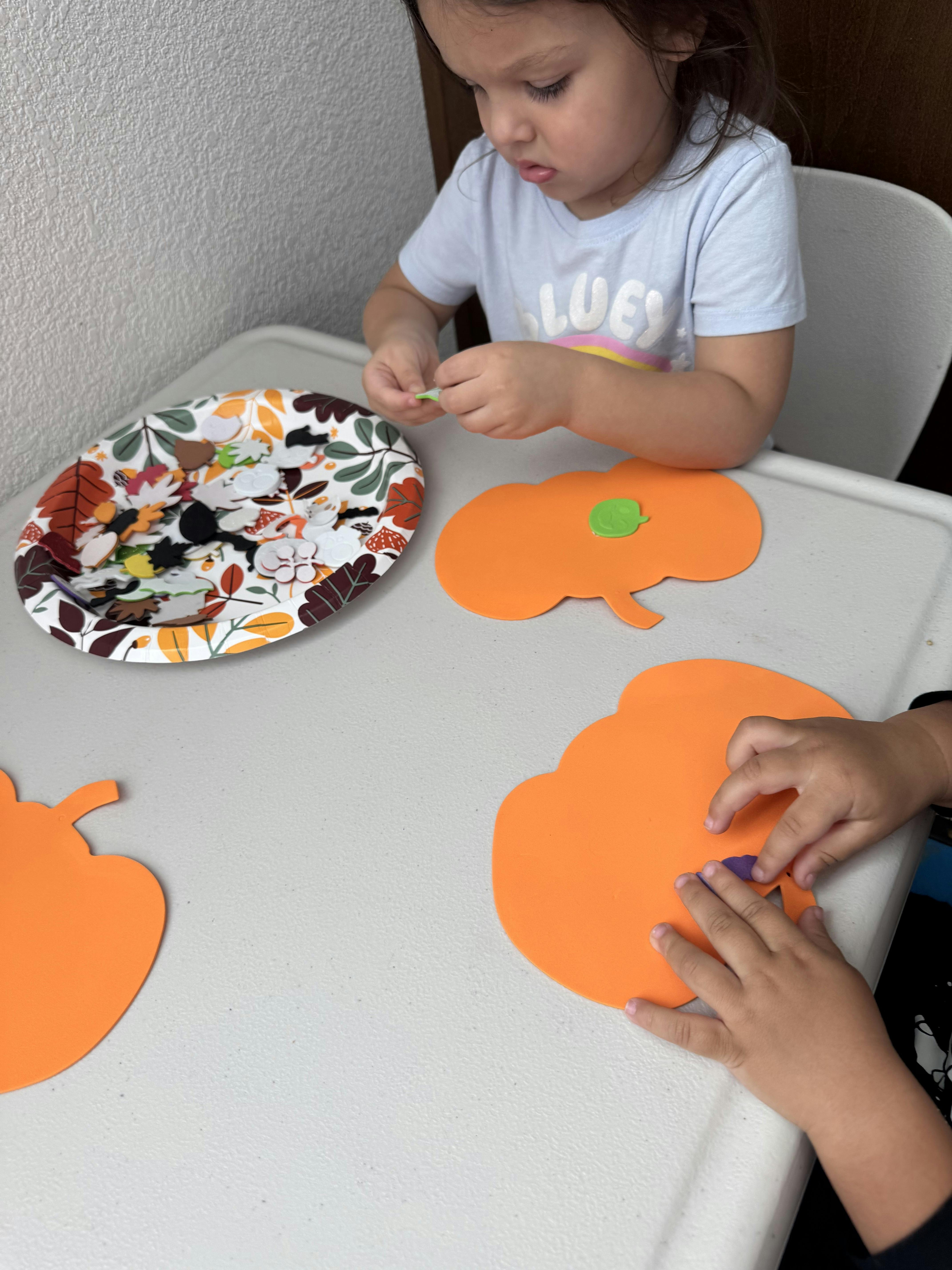 Children decorating orange pumpkin cutouts with small foam stickers