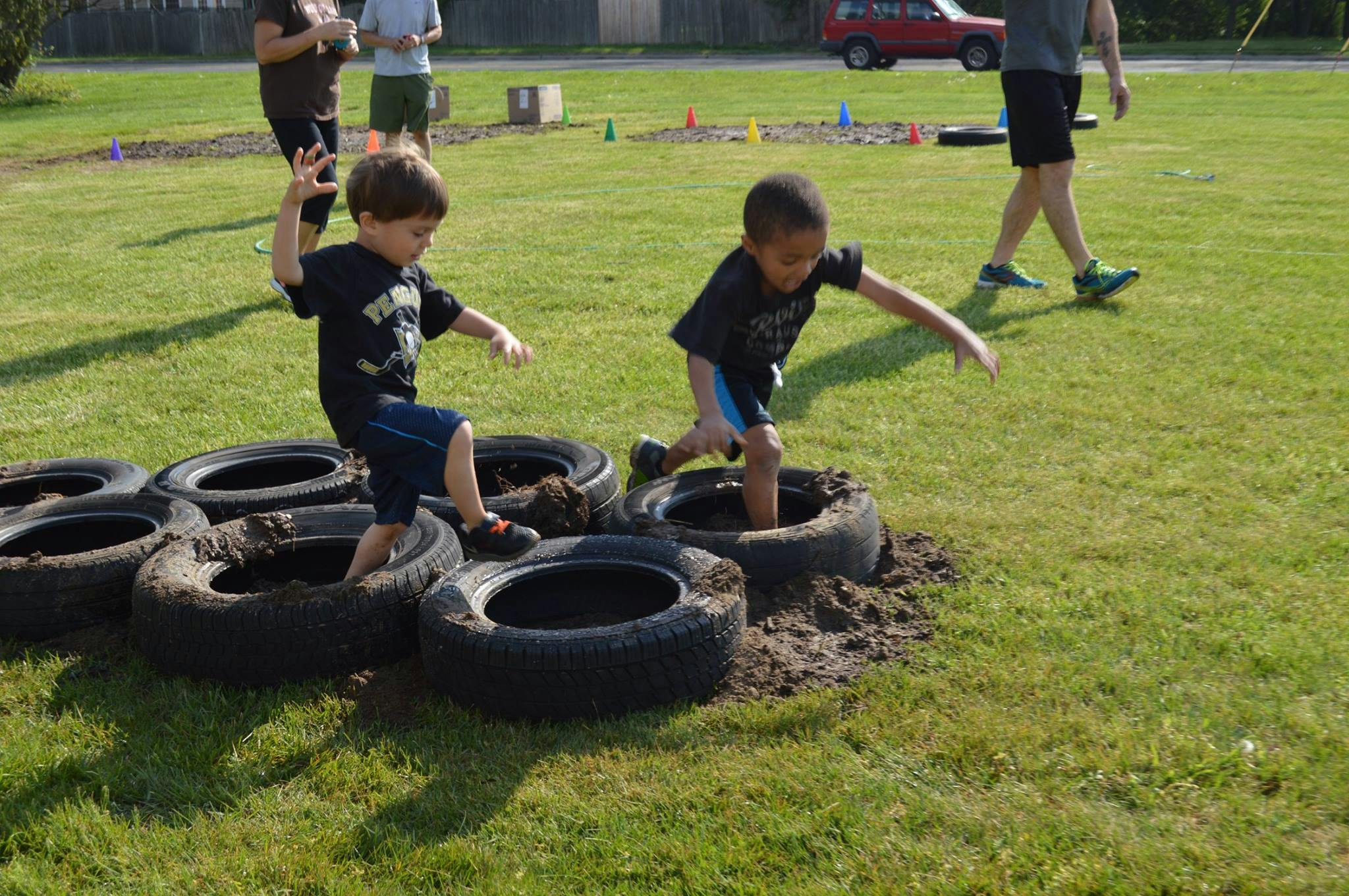 Two children stepping through tires on a grassy field