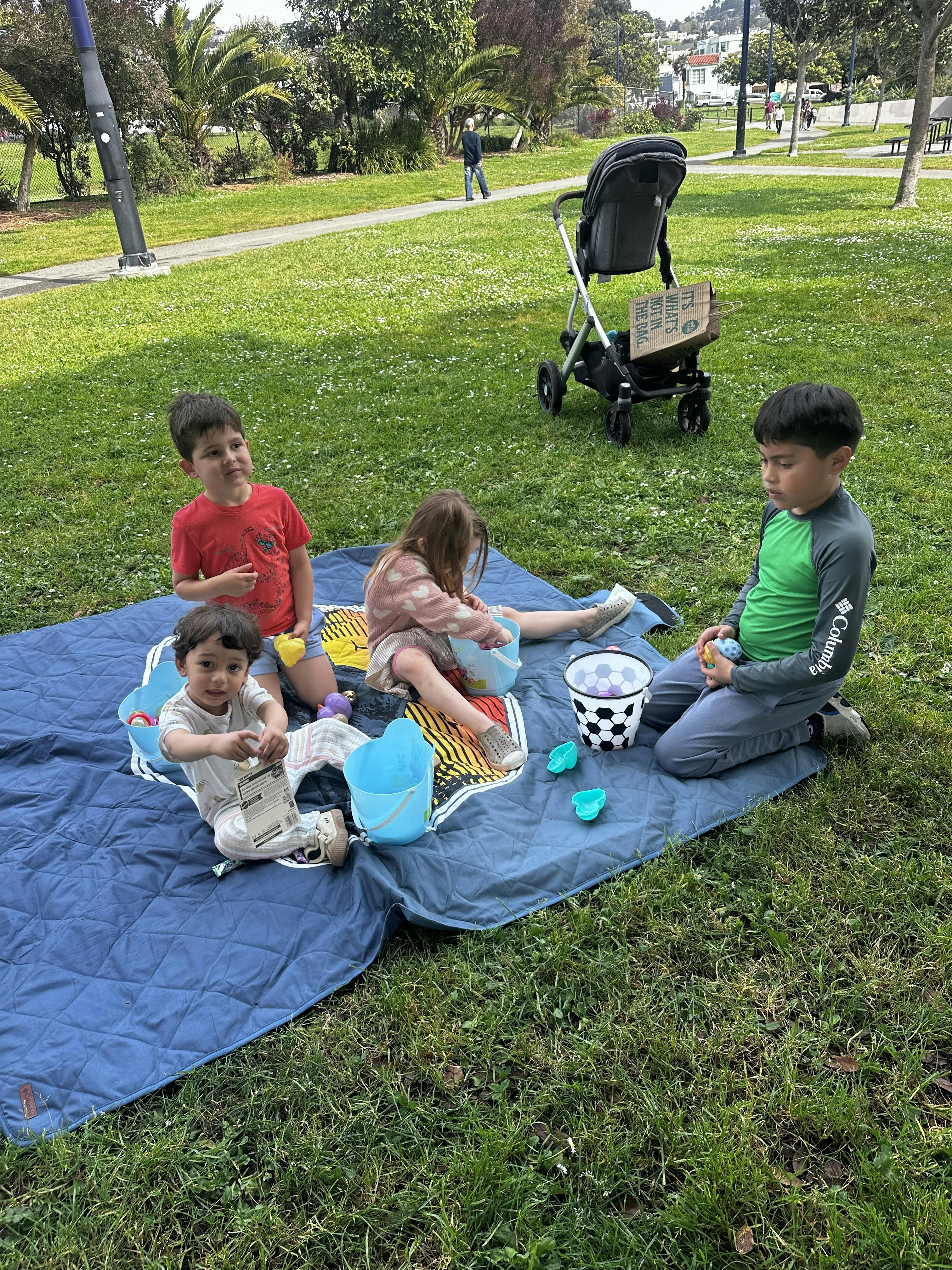 Four children playing on a blue blanket in a grassy park