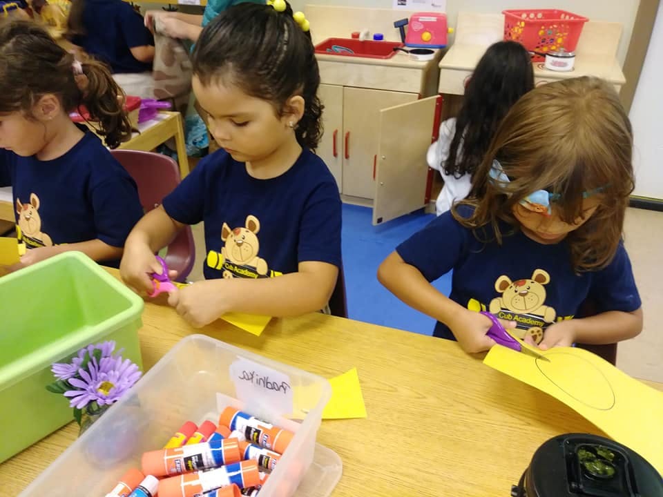 Children cutting paper at a table in a classroom
