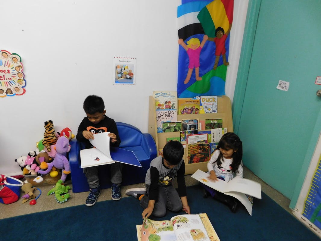 Three children reading books in a classroom