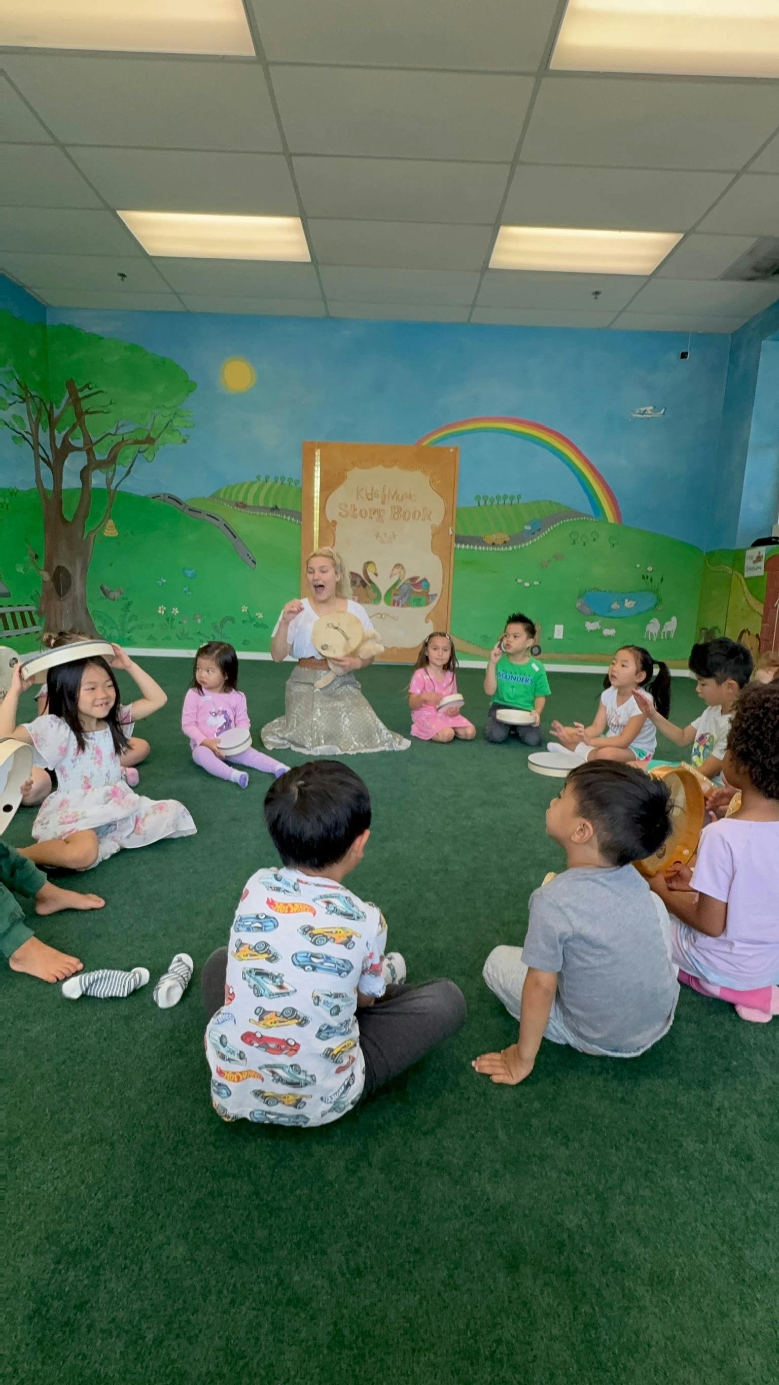 A person reading to a group of children sitting in a circle on a green floor