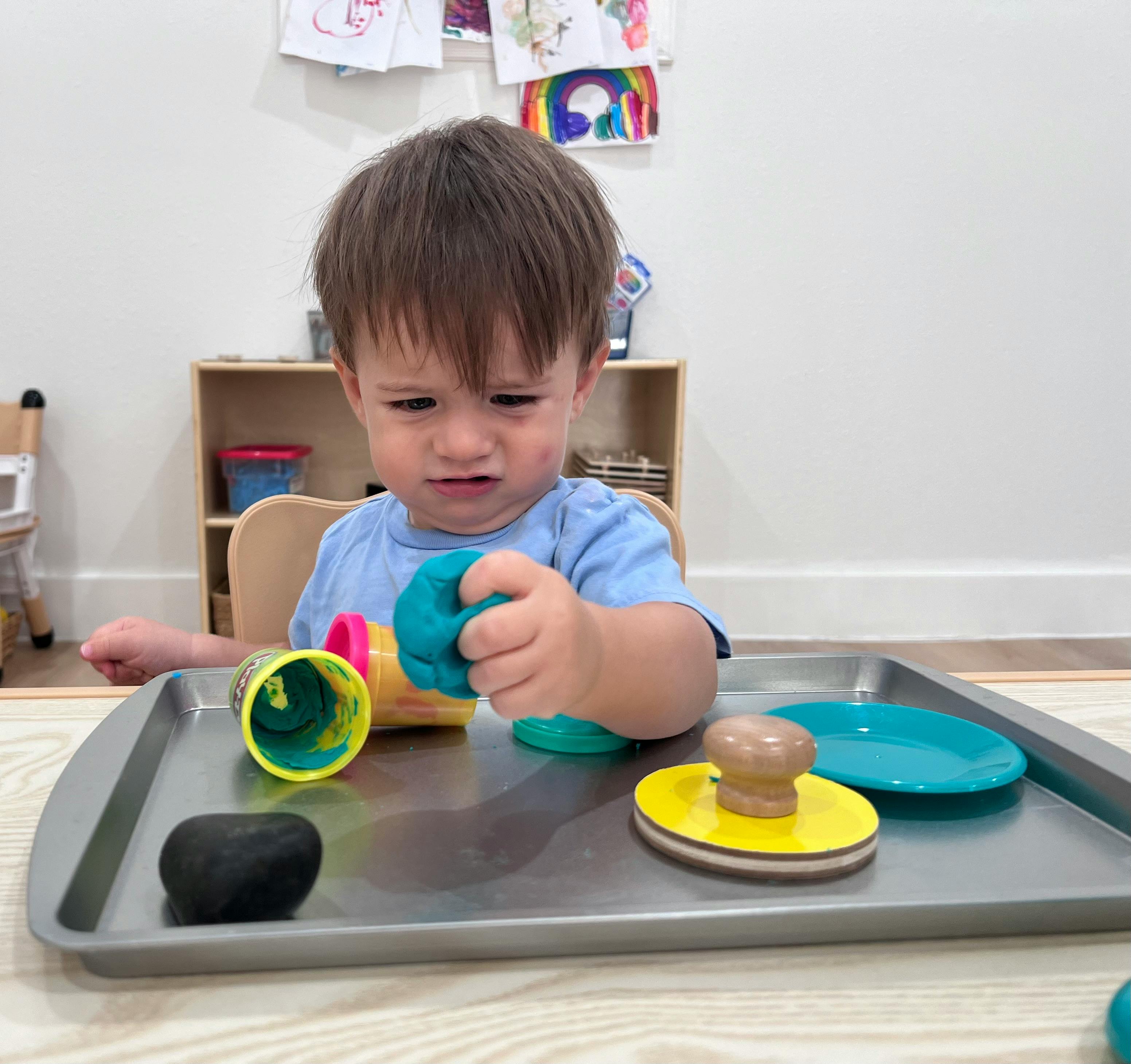 Child playing with modeling clay and tools on a tray