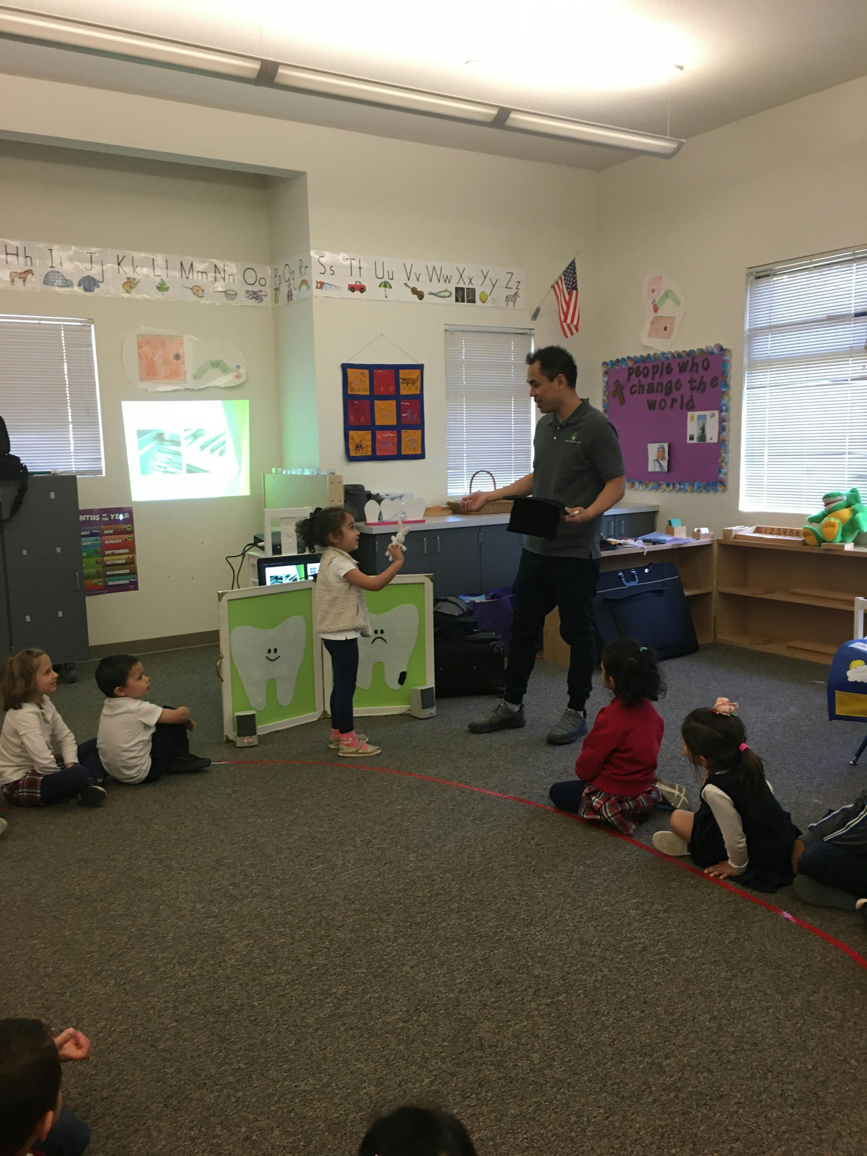 Adult and child interacting in a classroom with other children sitting on the floor