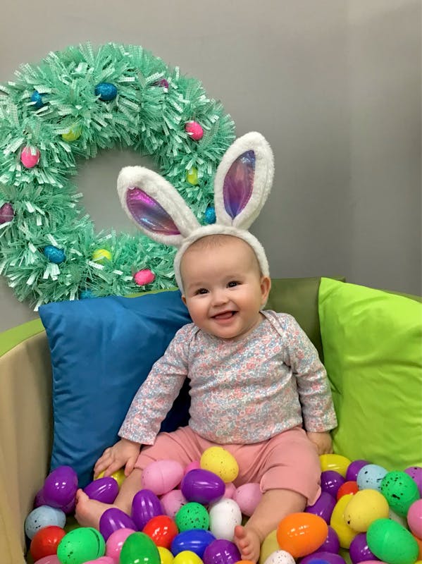 Child wearing bunny ears sitting in a pile of colorful plastic eggs