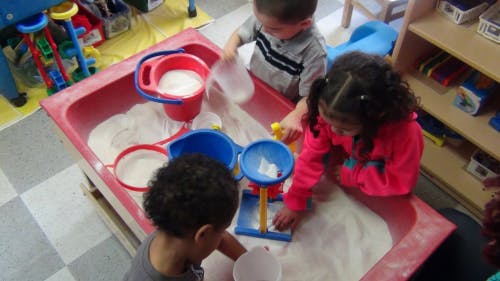 Three children playing with sand and toys in a sand table