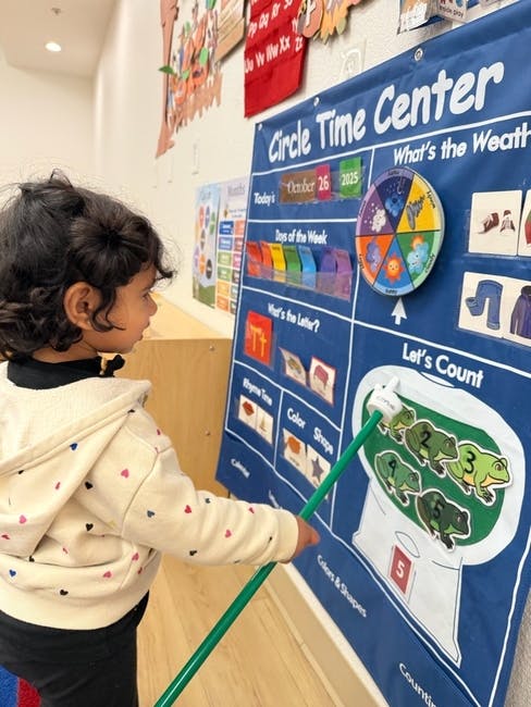 Child pointing at a "Circle Time Center" board with a stick