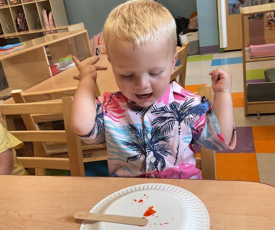 Child in a tropical shirt looking at a plate with a craft stick
