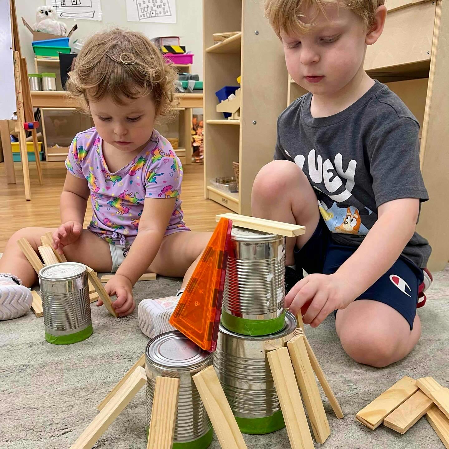 Two children playing with cans and wooden blocks on the floor