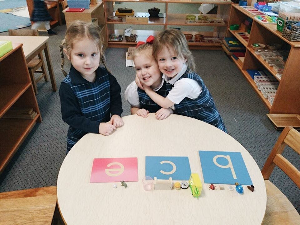 Three children standing around a table with letter cards in a classroom