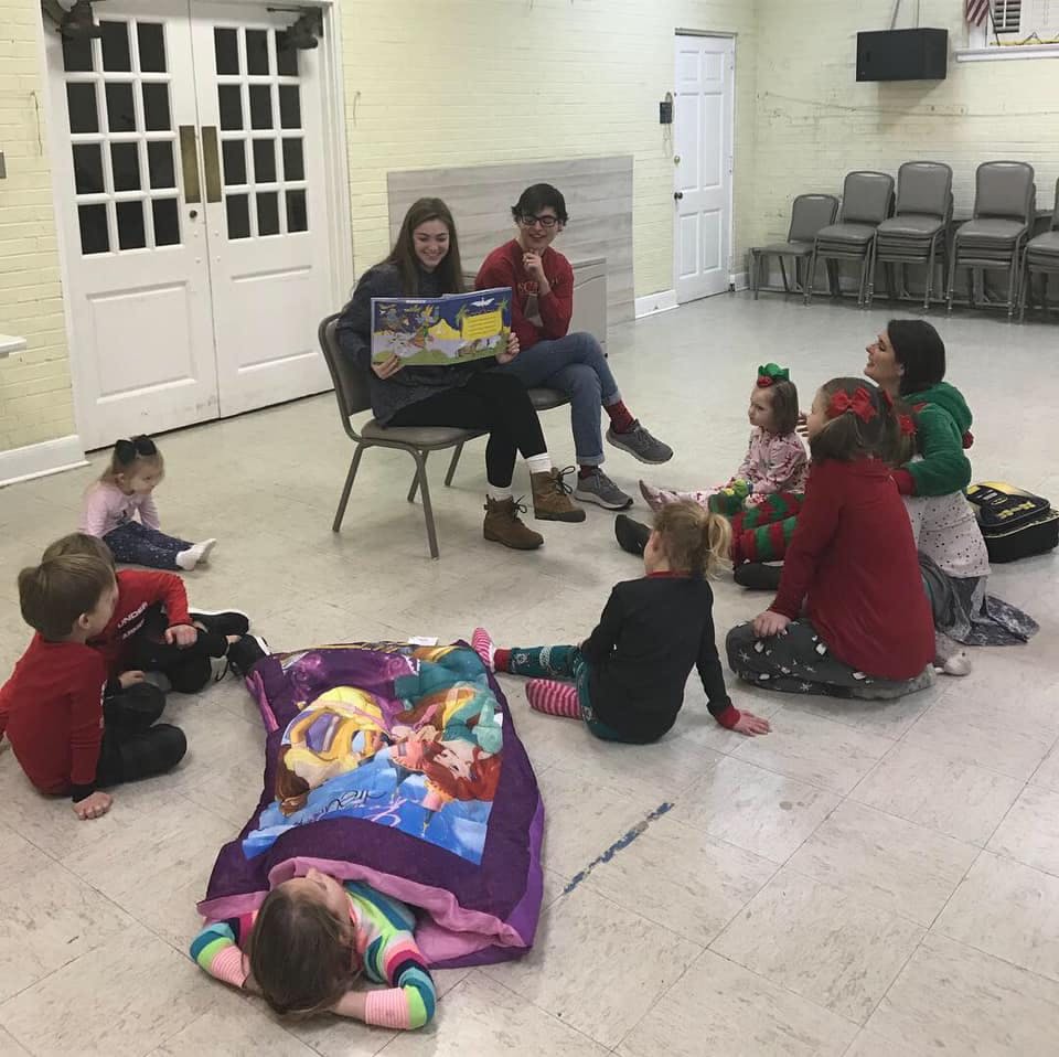 Two people reading a book to a group of children sitting on the floor