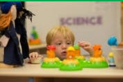 Child playing with a toy on a table, with "SCIENCE" in the background