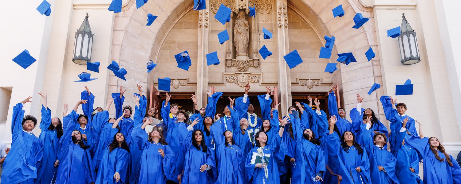 People in blue graduation gowns tossing their caps into the air