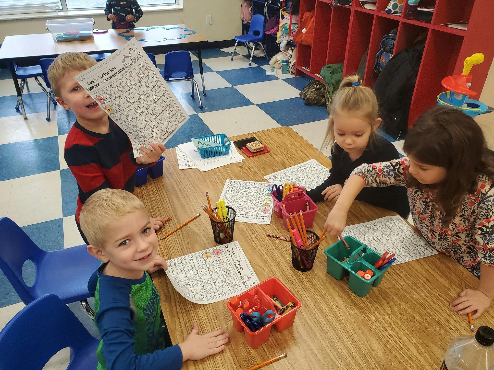 Four children sitting at a table with papers and art supplies