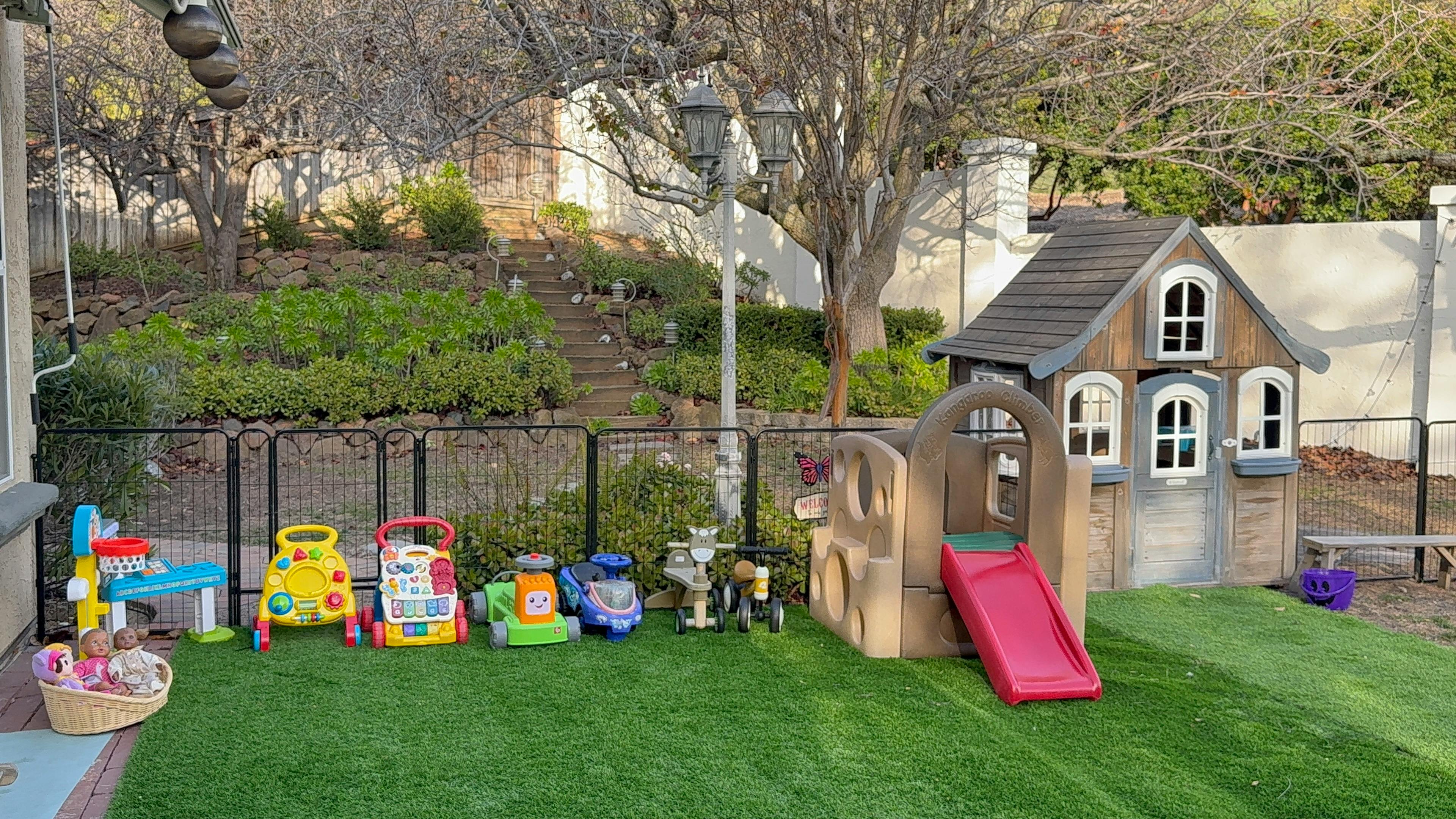 backyard with playhouse, slide, and various toys on artificial grass