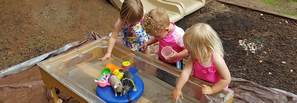 Three children playing with water and toys in a water table