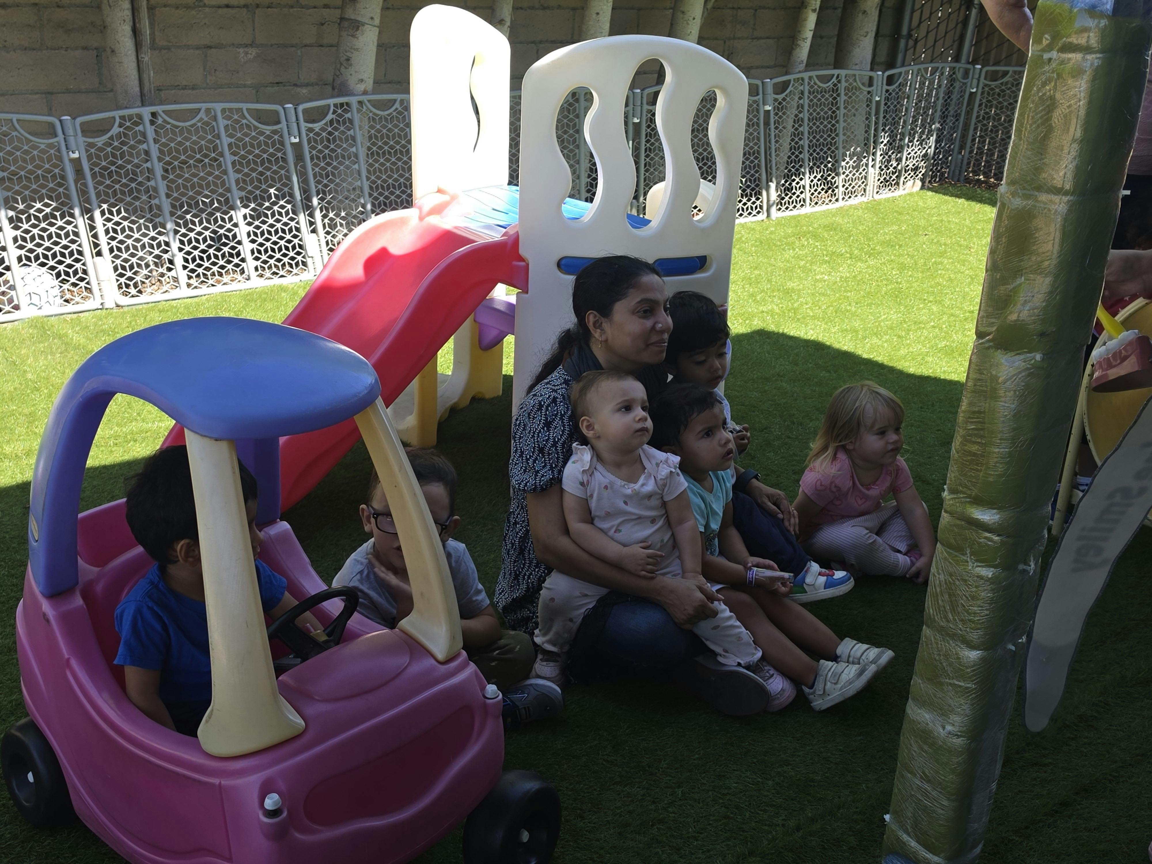 Adult and children sitting together on grass near playground equipment