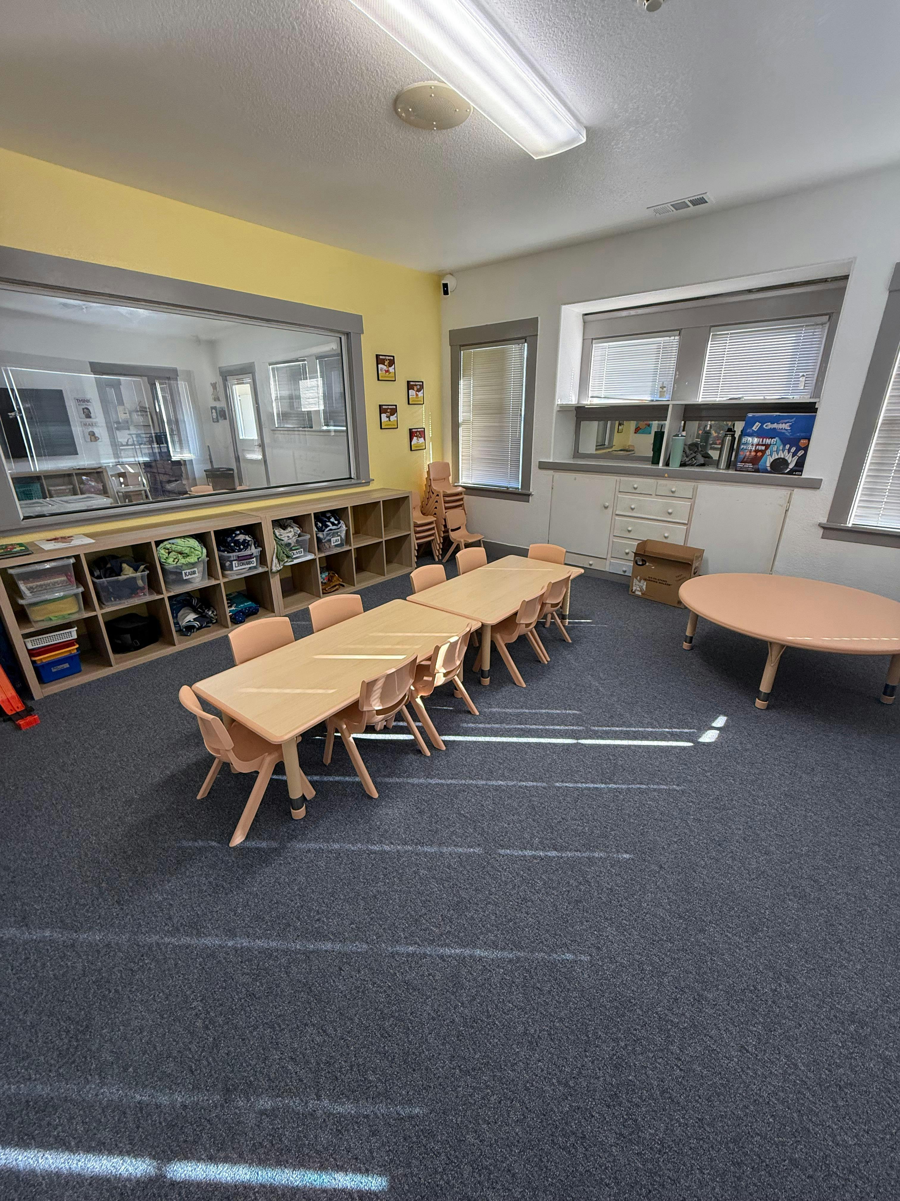 Classroom with child-sized tables and chairs, shelving units, and windows