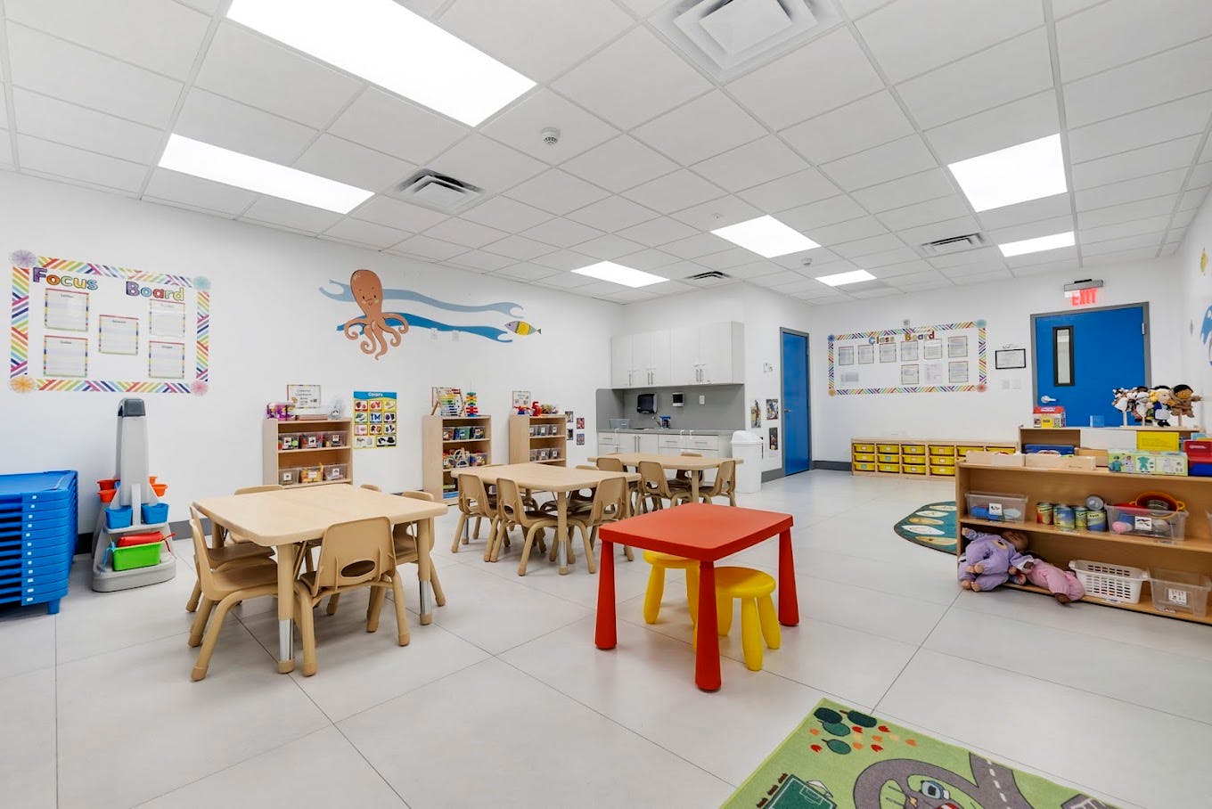 Classroom with small tables and chairs, shelves with toys, and wall decorations