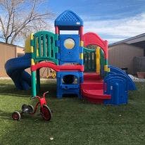 Colorful playground structure with a red tricycle on artificial turf