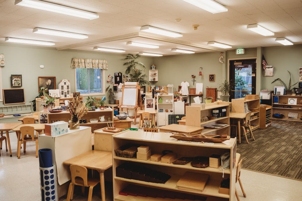 Classroom with small wooden tables, chairs, and shelves