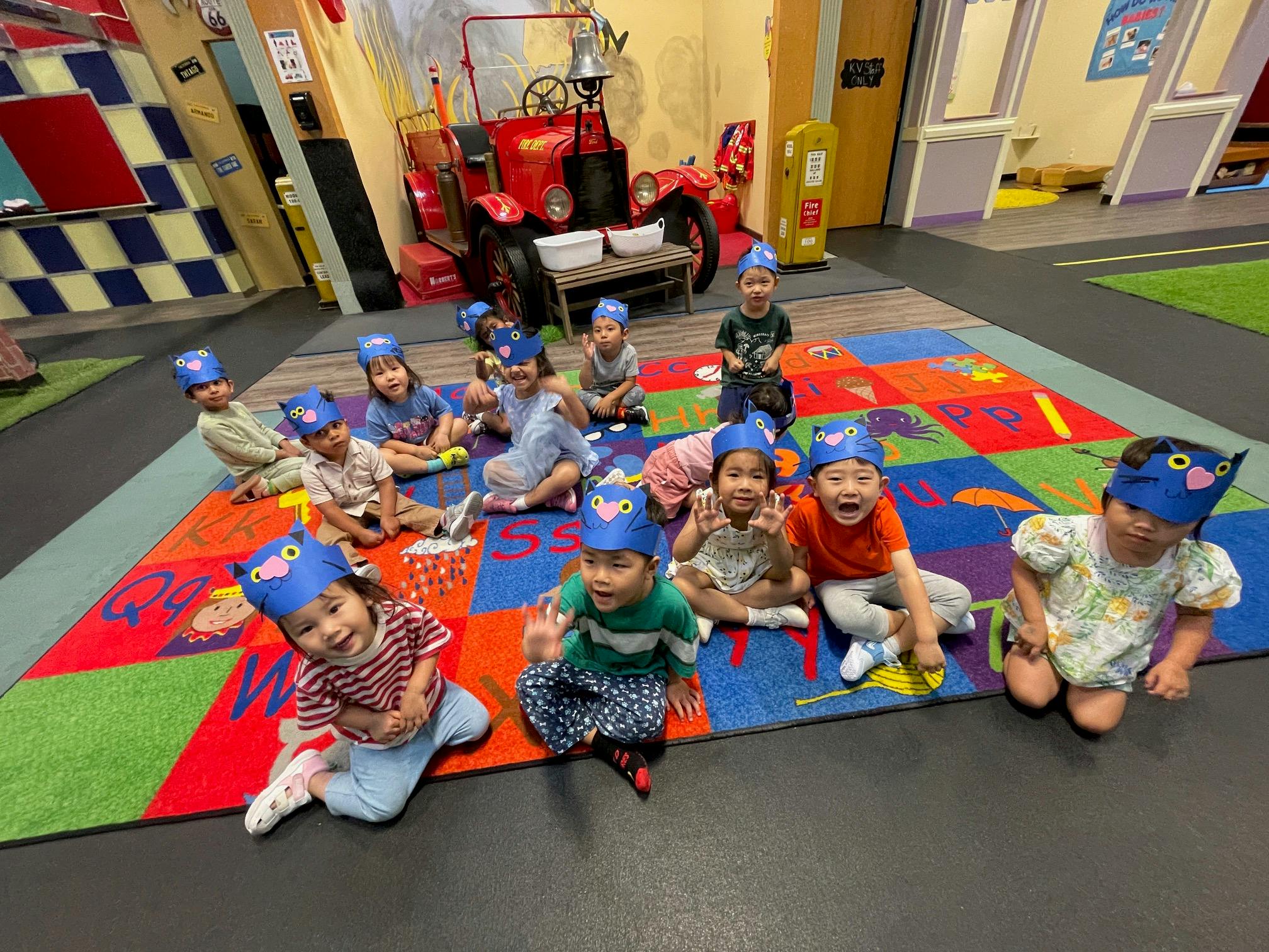 Group of children wearing blue hats sitting on a colorful rug in a classroom