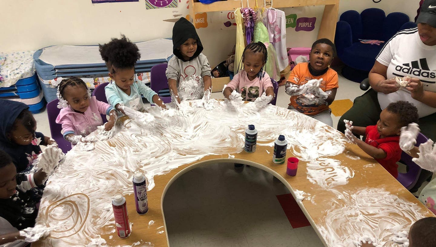 Children and an adult playing with shaving cream on a table