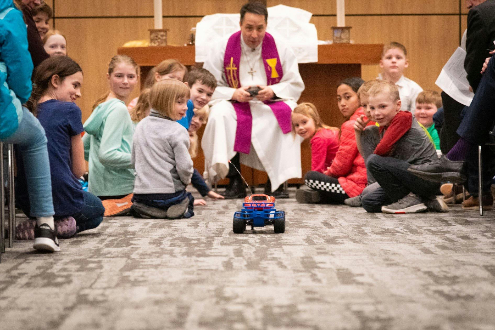 Person in religious vestments with children watching a remote control car