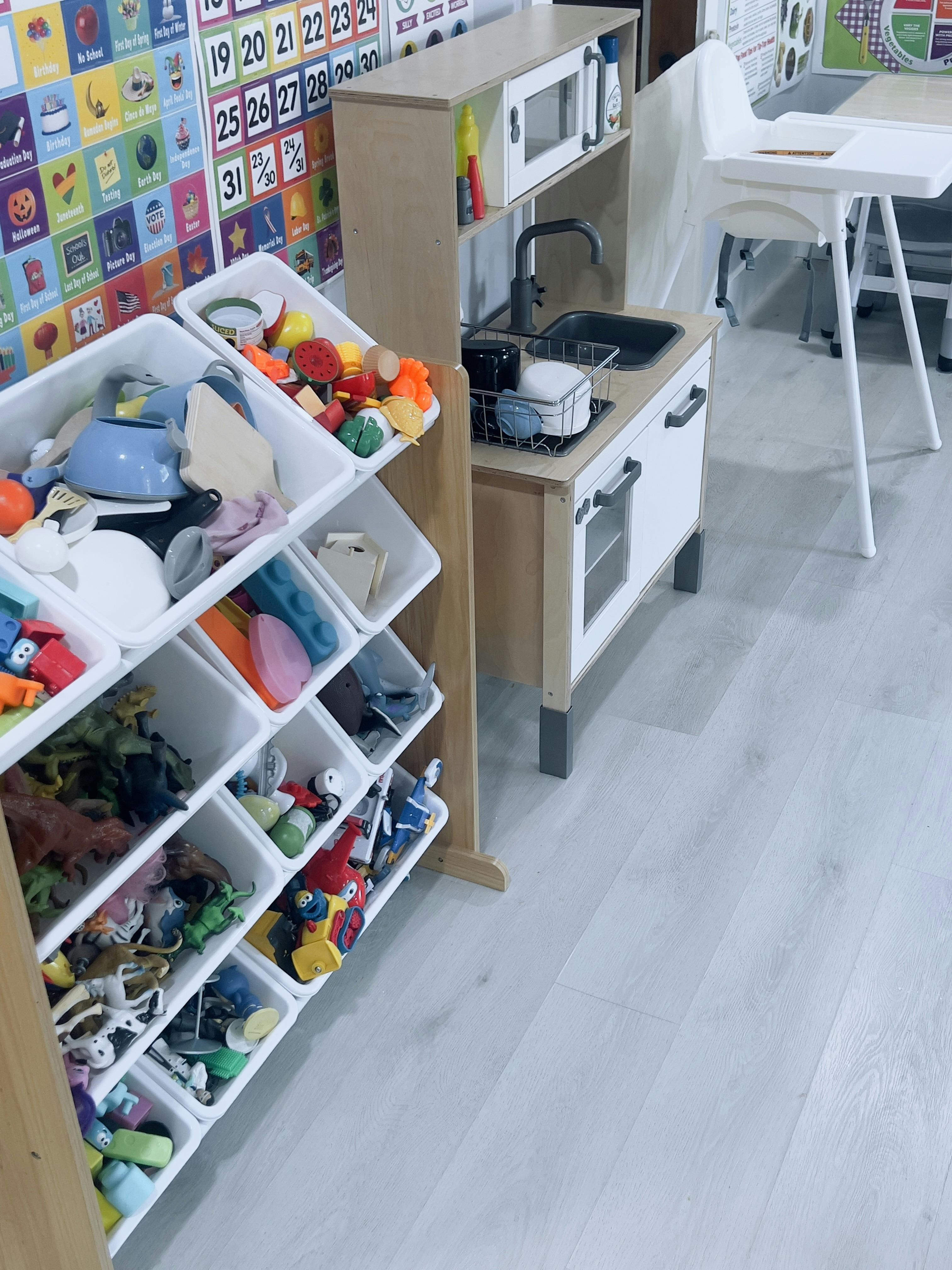 Toy storage bins filled with play figures next to a toy kitchen in a playroom