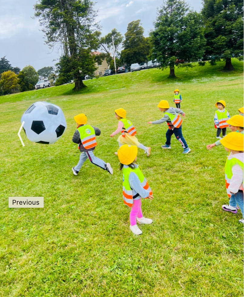 Children wearing yellow hats and safety vests playing with a large soccer ball