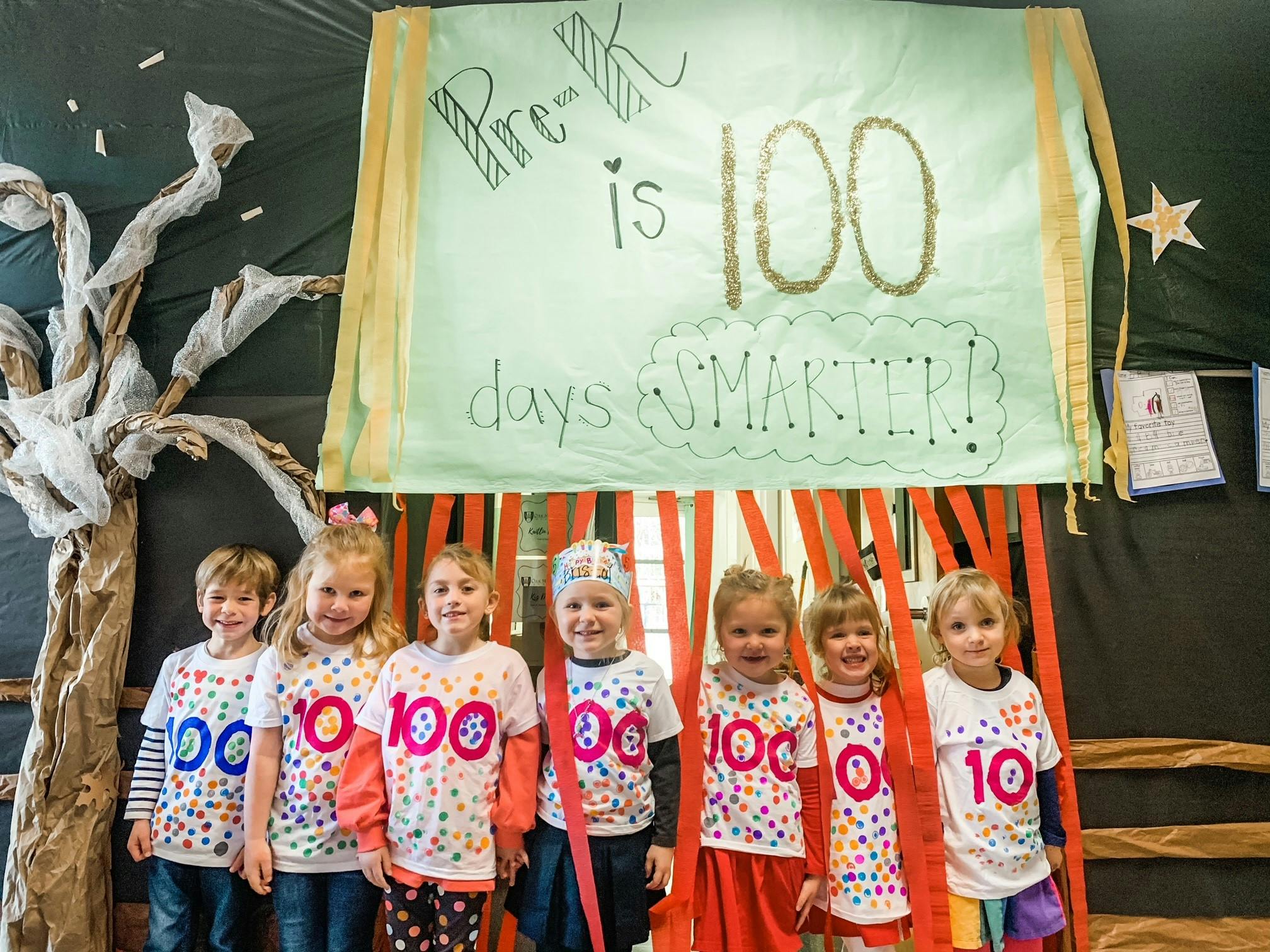 Six children standing in front of a banner that reads "Pre-K is 100 days SMARTER!"