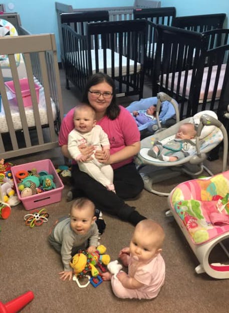 Person holding a baby, with other babies and cribs in a room