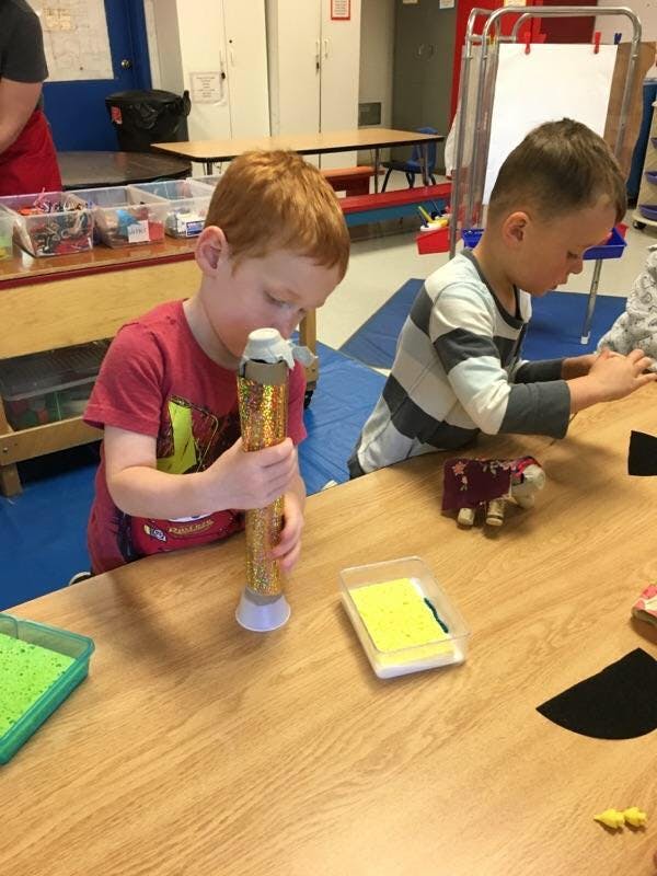 Two children at a table, one holding a glittery tube, the other looking down