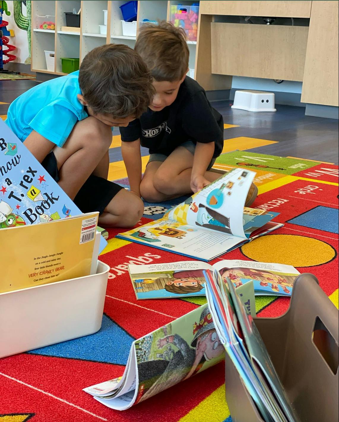 Two children kneeling on a rug looking at books
