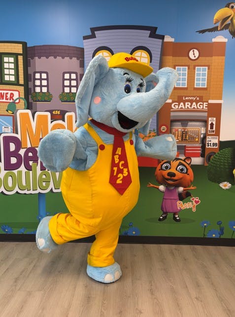 Elephant mascot in yellow overalls and red tie with ABC 123 text