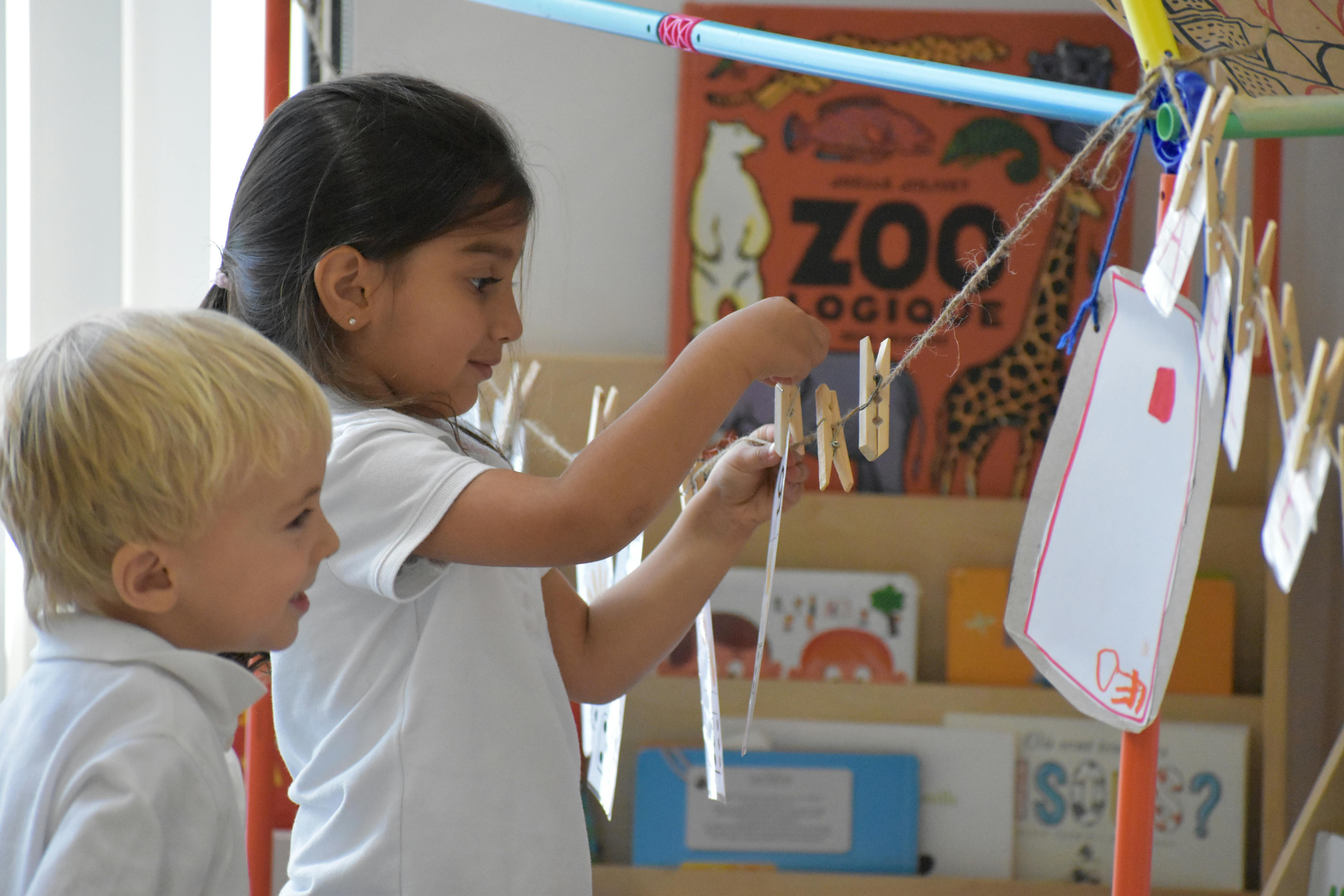 Child hanging paper on a line with clothespins, another child watching