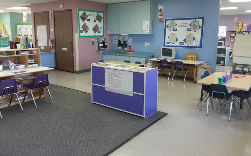 An empty classroom with small tables and chairs, computers, and colorful walls