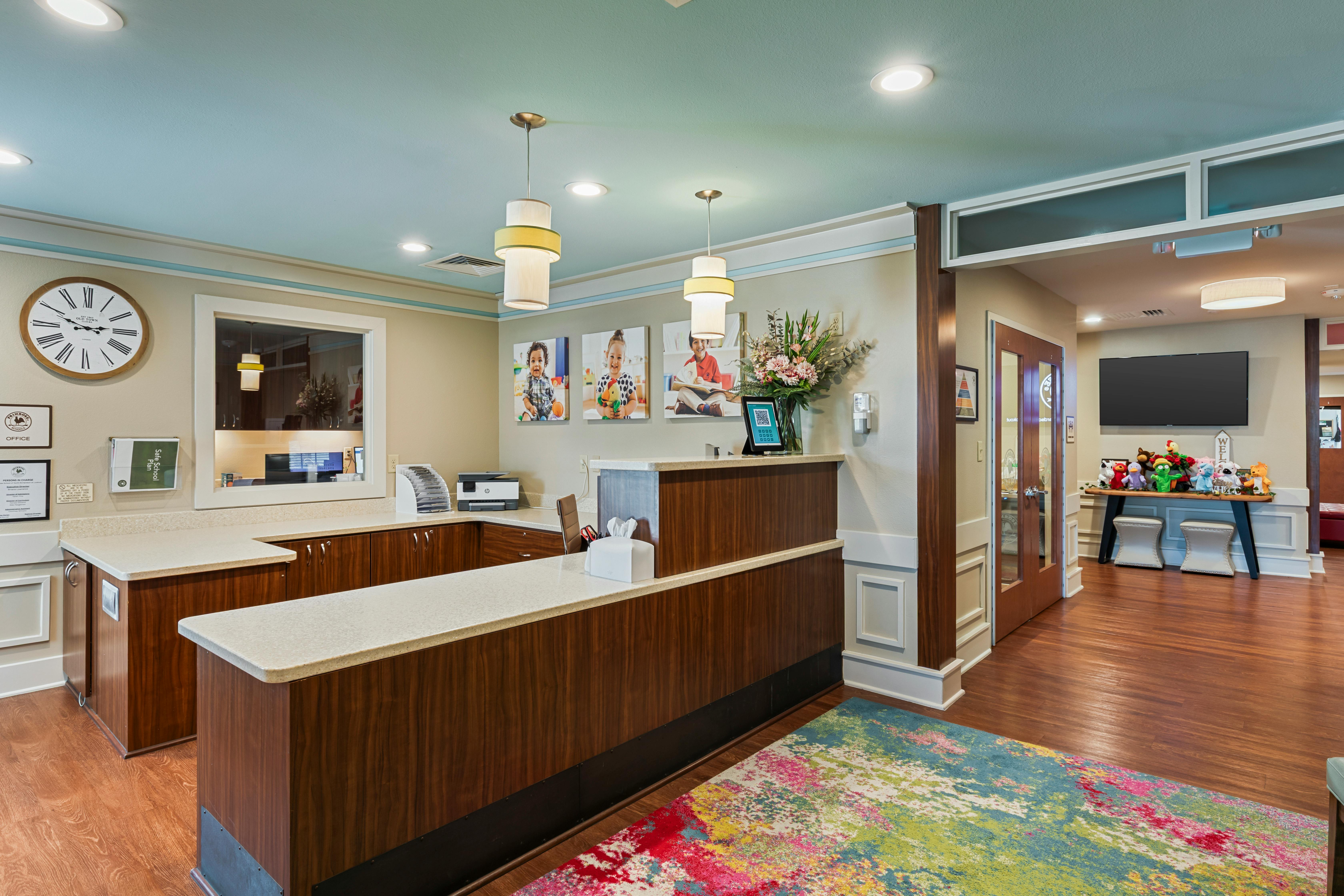 Reception desk with three photos of children on the wall and a bright rug