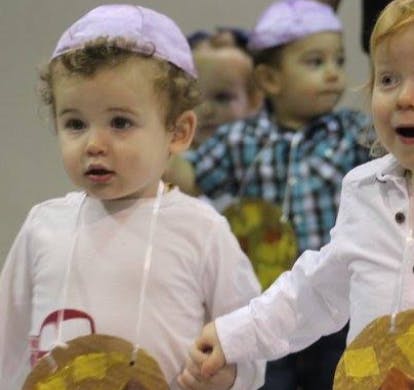 Two children holding hands, one wearing a purple cap