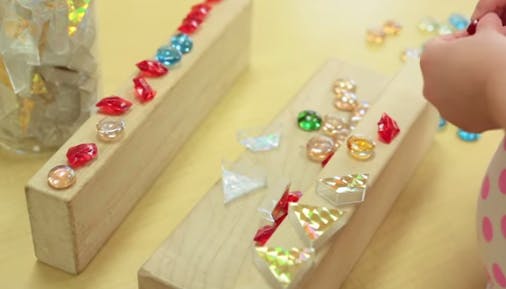 Child placing colorful gems on wooden blocks
