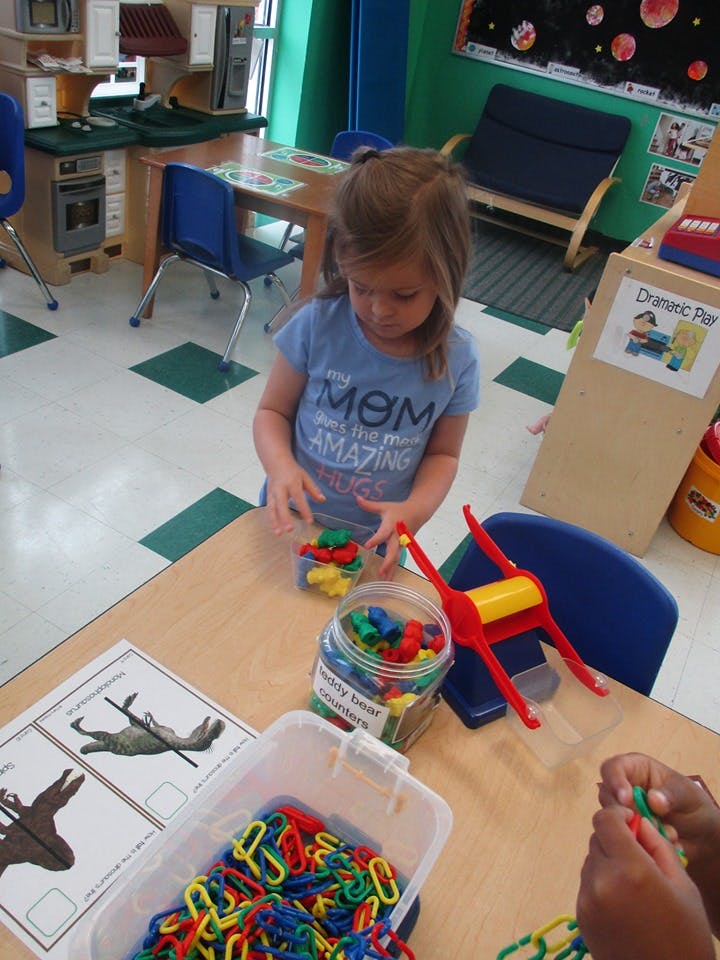 Child playing with colorful plastic links at a table in a classroom