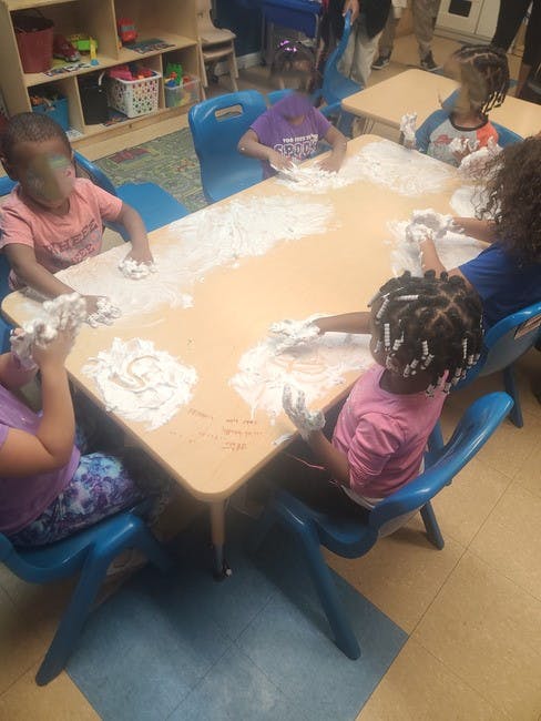 Children playing with white powder on a table in a classroom