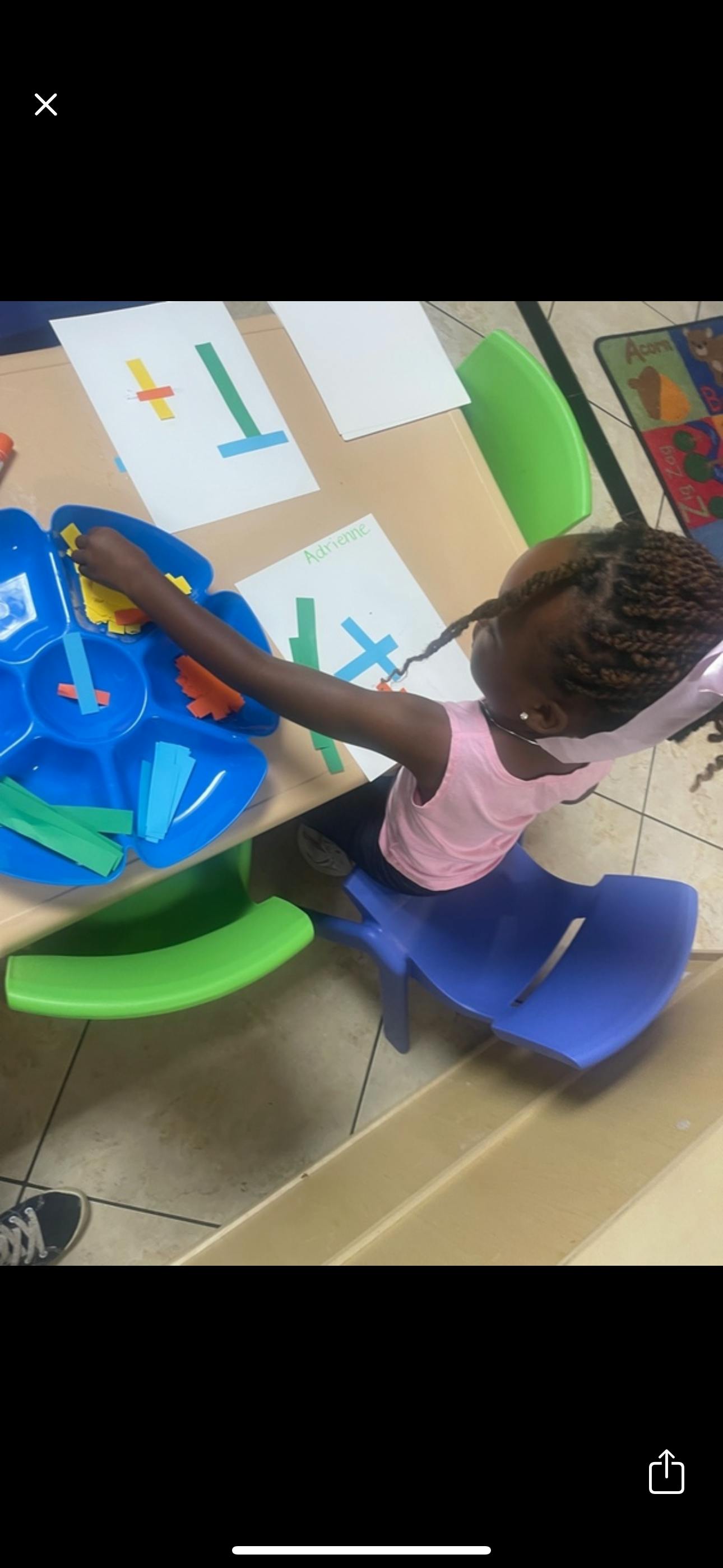 Child sitting at a table arranging paper shapes for an art activity