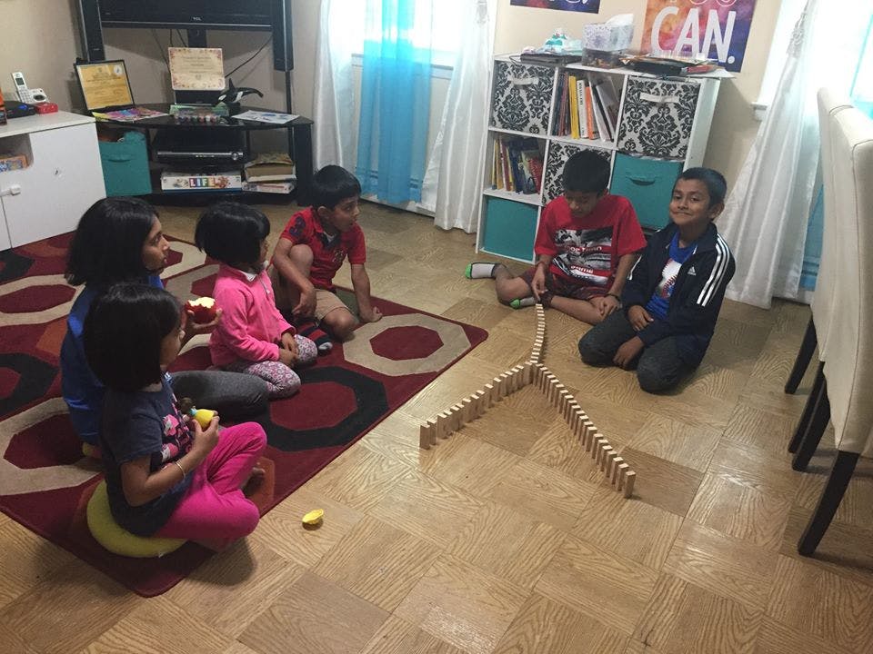 Children sitting on a rug and floor playing with dominoes