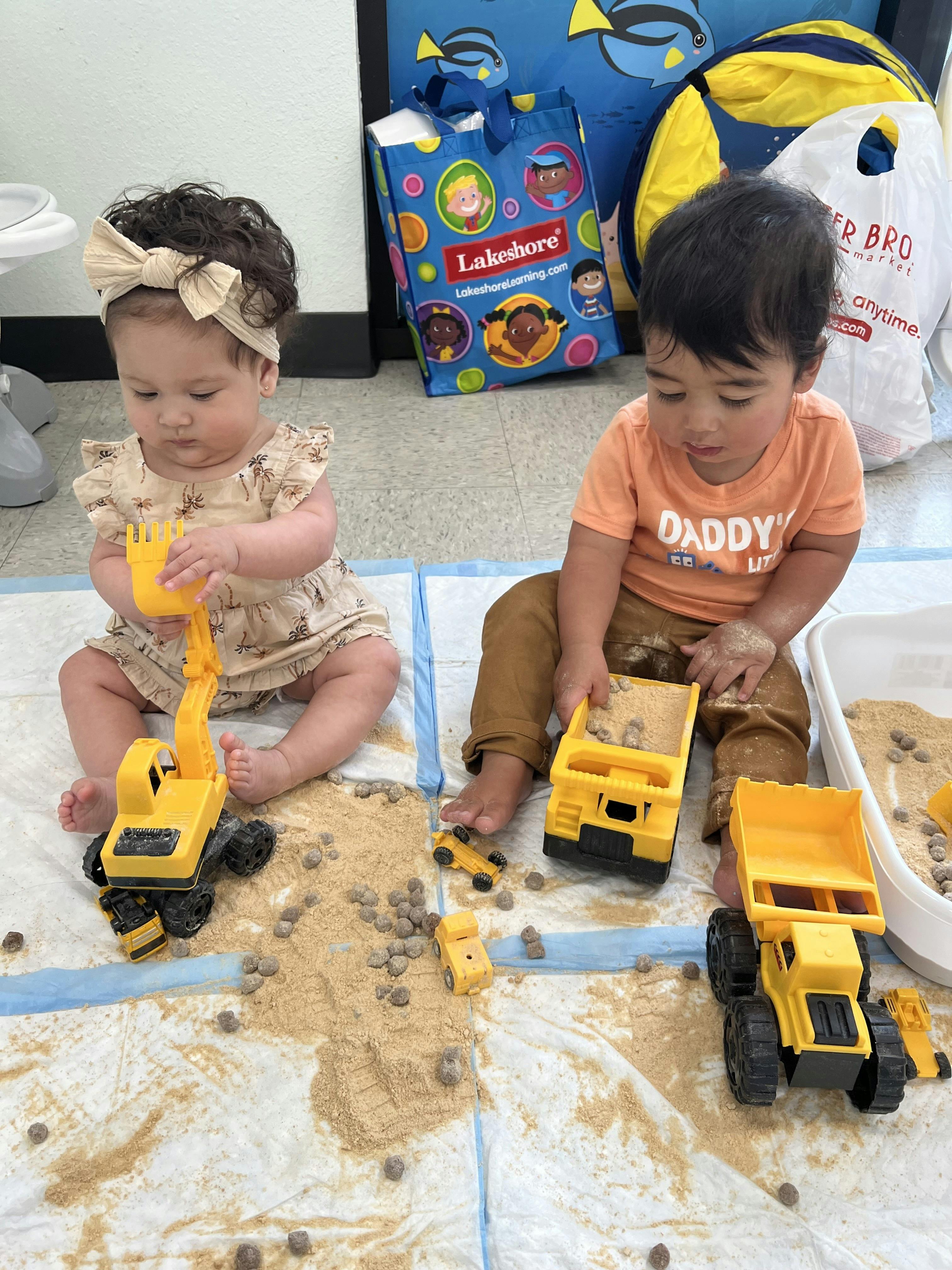 Two children playing with toy construction vehicles in sand