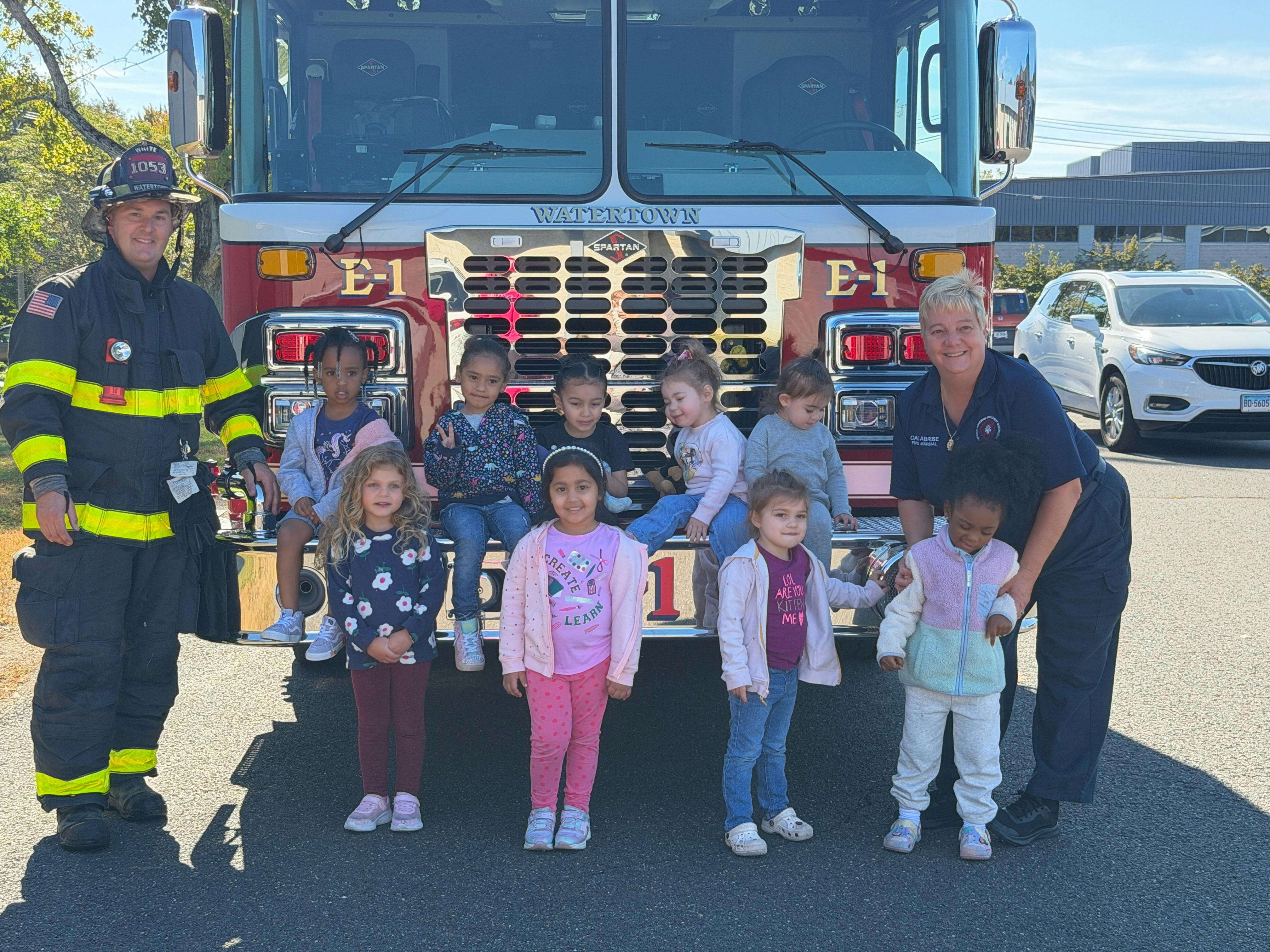 Two adults and multiple children posing in front of a fire truck