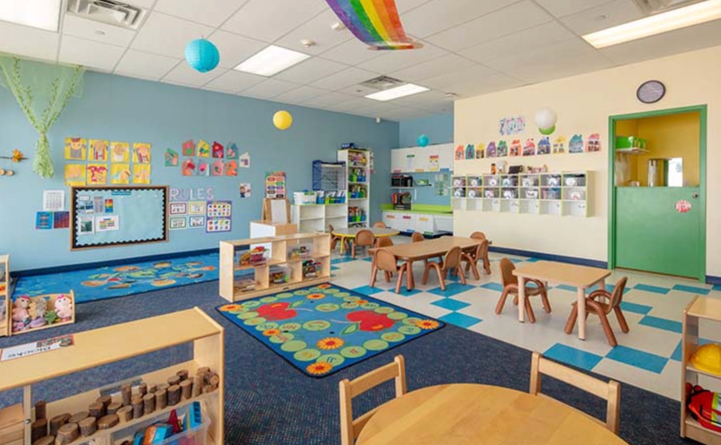 Empty classroom with small tables and chairs, colorful rugs, and decorations