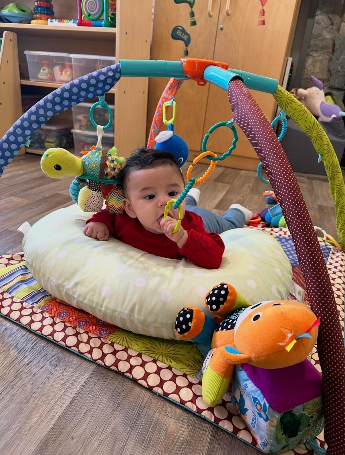 Child on a playmat, propped up by a pillow, playing with a teething toy